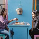 Mother and daughter enjoying a sunny day playing chess outdoors, fostering family bonding.